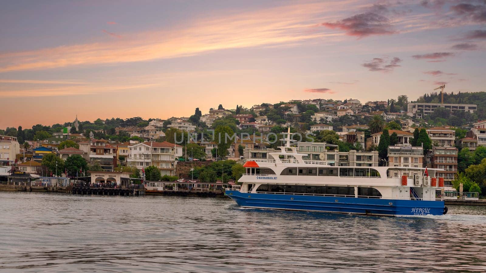 Istanbul, Turkey - August 25, 2022: Ferry boat in Marmara sea with background of the green mountains of Buyukada island, with traditional summer houses, trees, and ferry terminal on the far end