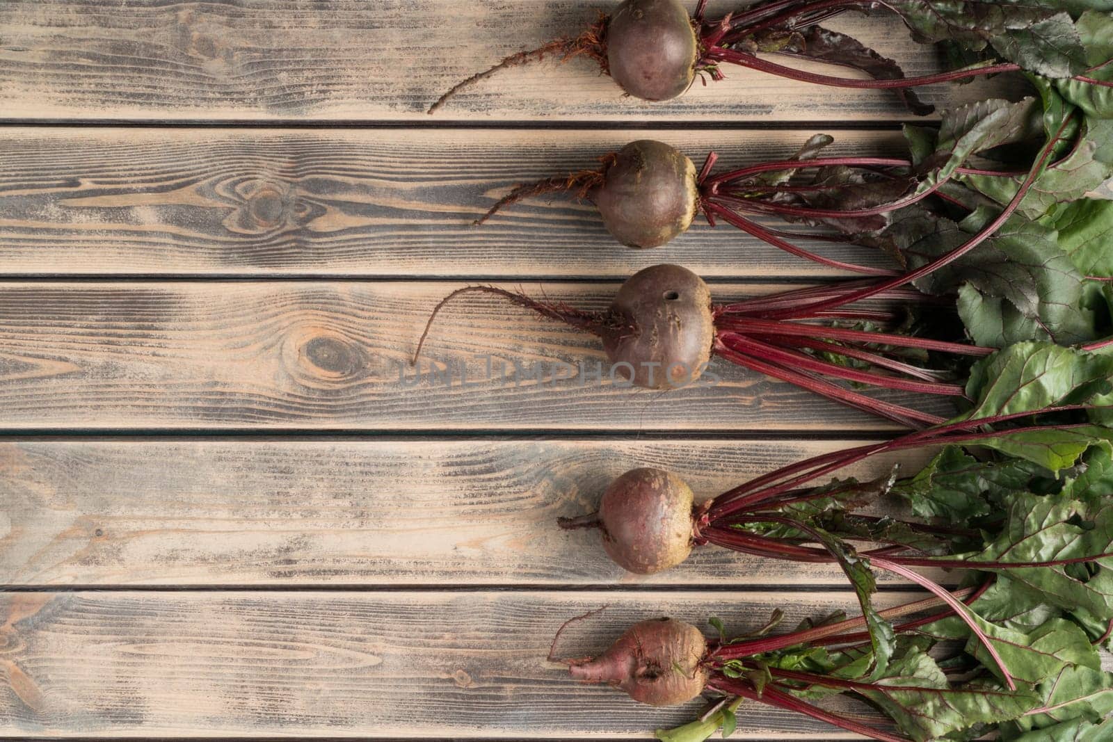 Layout of fresh, clean purple beet roots with stems and leaves on wooden background. Diet and healthy rustic seasonal food. Cooking, market produce and advertisement. Top view, flat lay, copy space