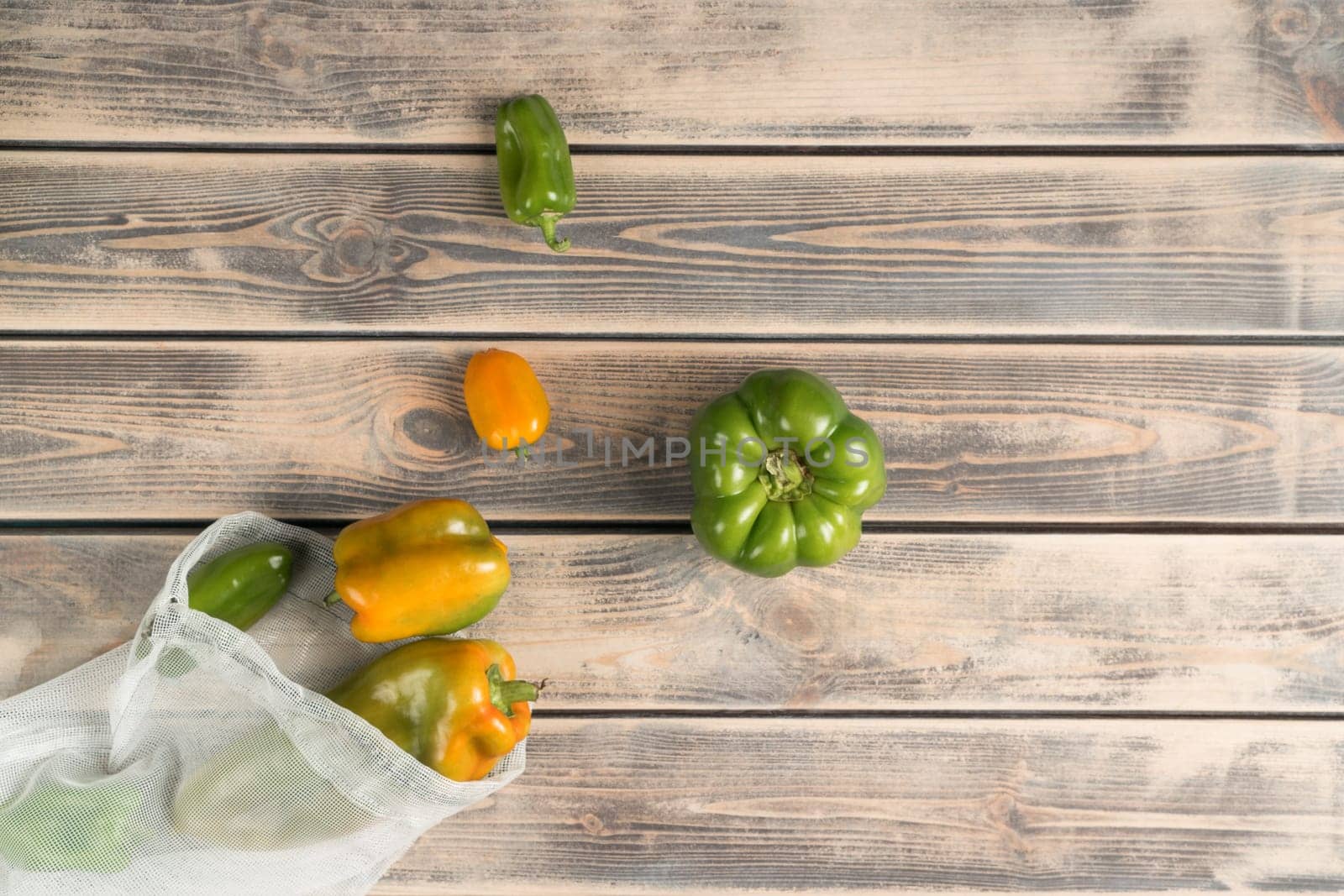 Food vegetable composition of fresh, juicy green and yellow bell peppers scattered from packet on wood background. Fresh healthy products in natural material package. Top view, above, copy space