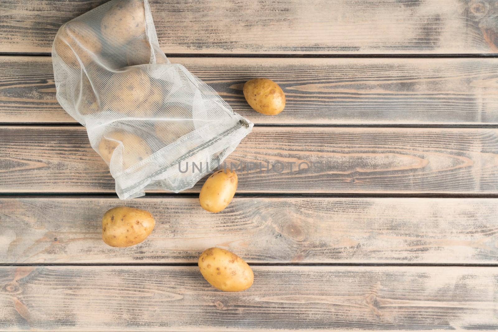 Composition of raw fresh potato in transparent packet on wooden background. Degradable package, zero waste and ecological, sustainable lifestyle. Zip pack, bio organic material. Top view, copy space