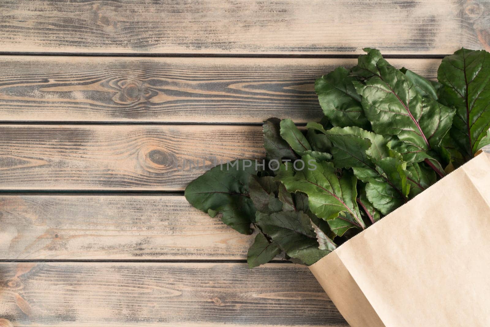 Lush green foliage and stems of beet roots hiding in eco bag, package on wooden background. Ecological shopping, food delivery and organic farm vegetable market, store. Top view, copy space