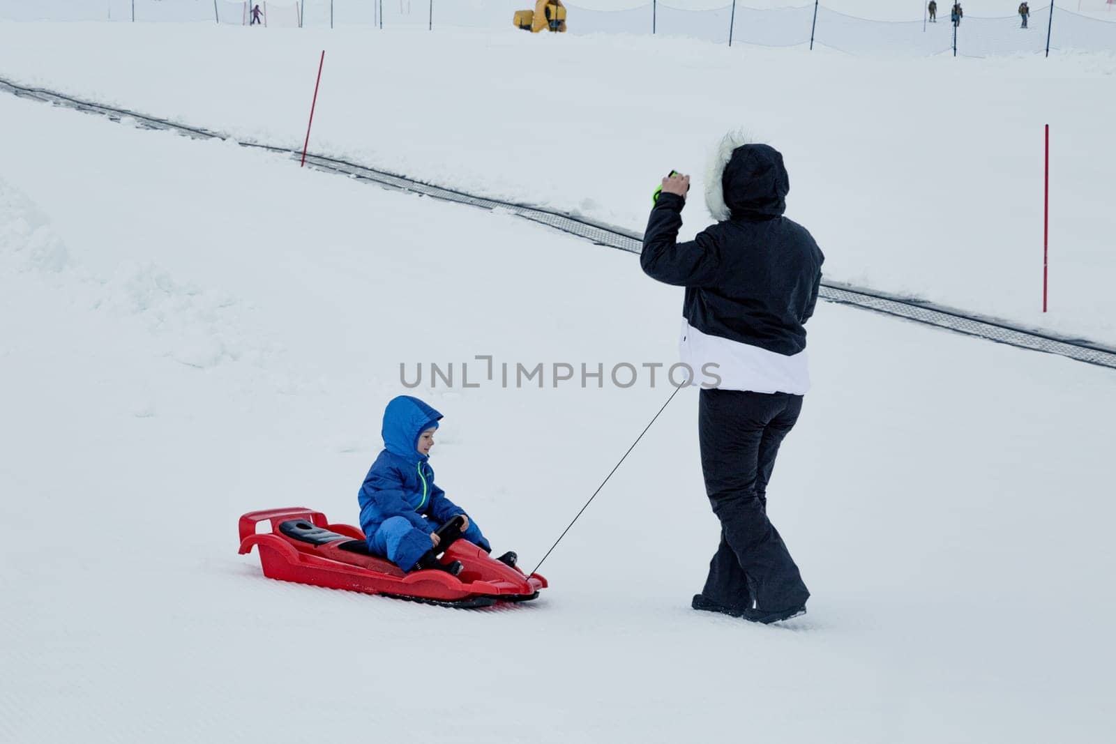 Mom and baby enjoy a sleigh ride. Sledding for children. Child riding a sleigh. Children play outdoors in the snow. Outdoor fun for family Christmas holidays.