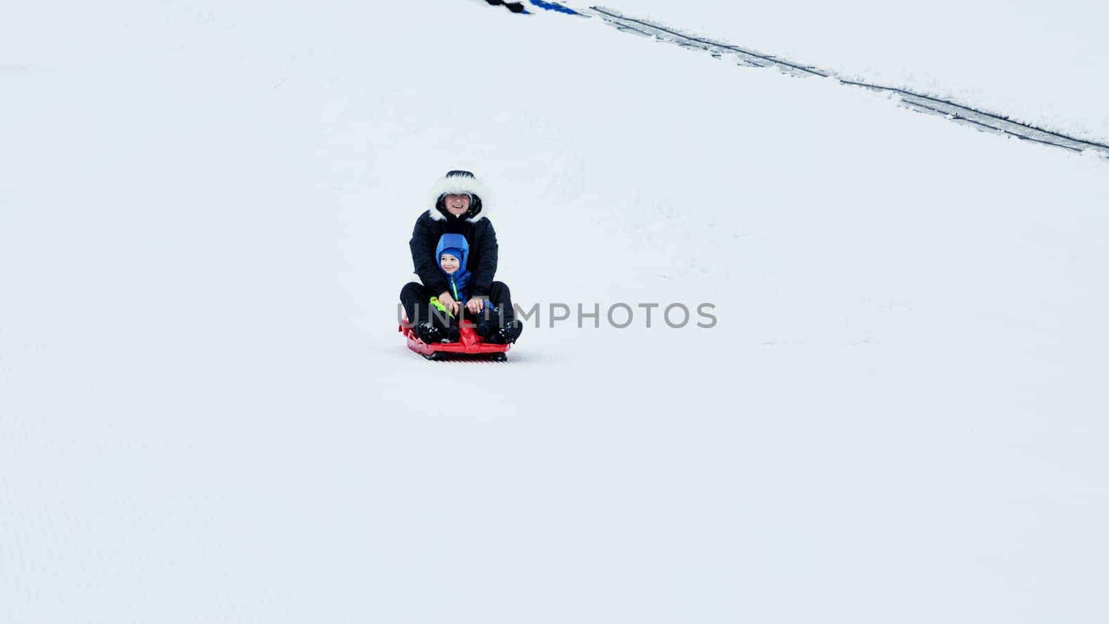 Mom and baby enjoy a sleigh ride. Sledding for children. Child riding a sleigh. Children play outdoors in the snow. Outdoor fun for family Christmas holidays.