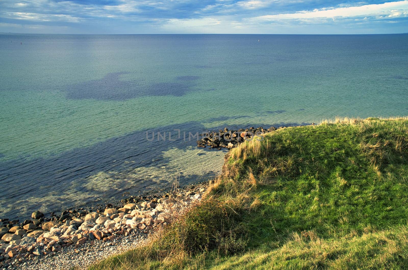 Hundested, Denmark on the cliff overlooking the sea. Baltic Sea coast, grassy meadow, beach. Clouds on horizon. Landscape photo from Scandinavia.
