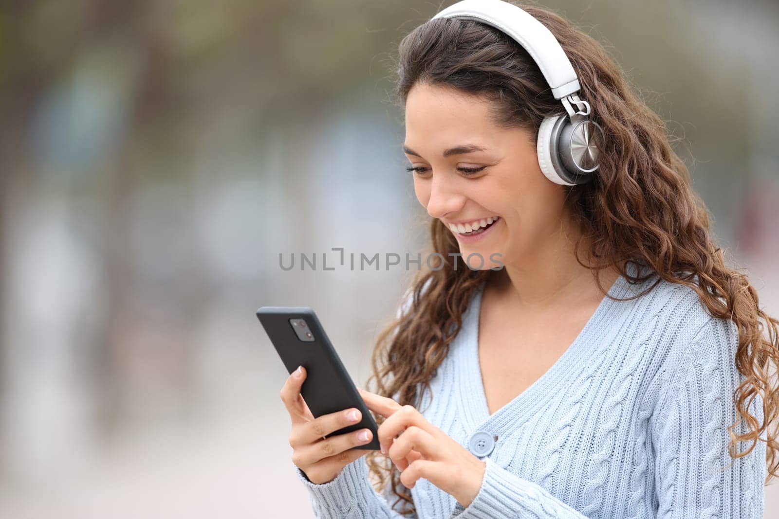 Happy woman walks listening to music checking phone in the street