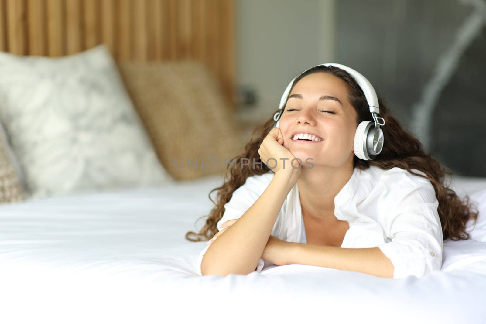 Happy woman on the bed listening to music with headphones in the bedroom