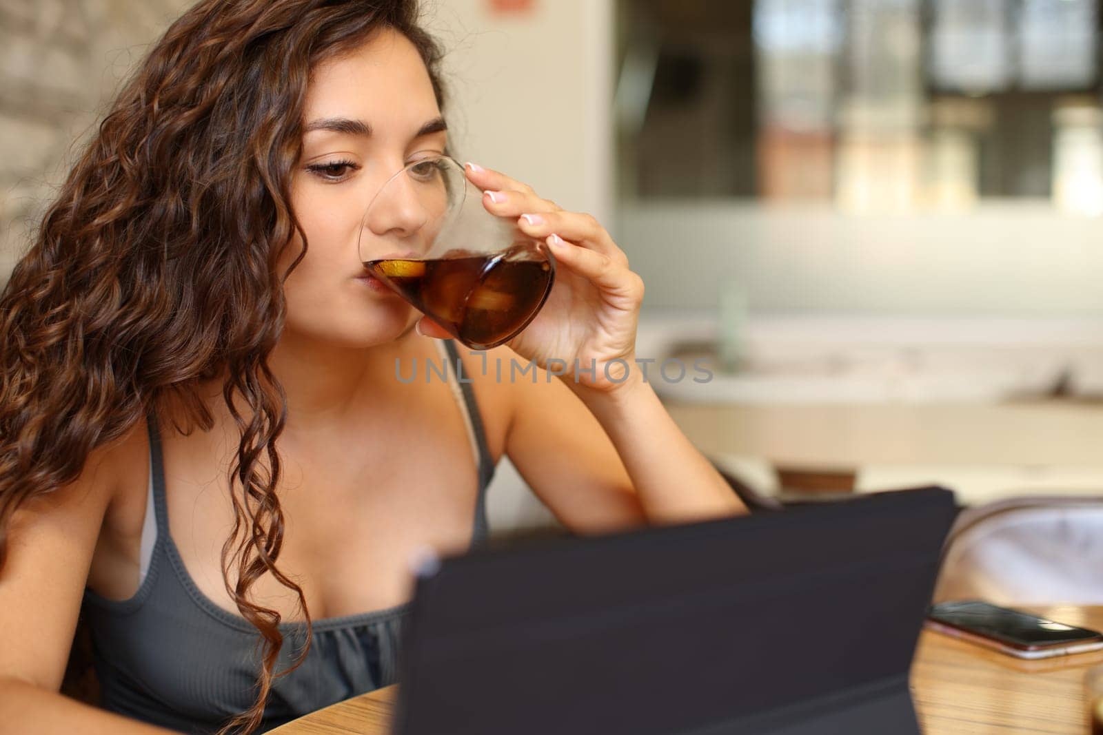 Woman drinking soda and checking tablet sitting in a bar