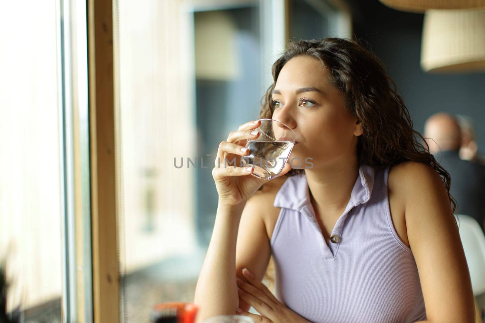 Distracted woman drinking water in a restaurant looking away through a window