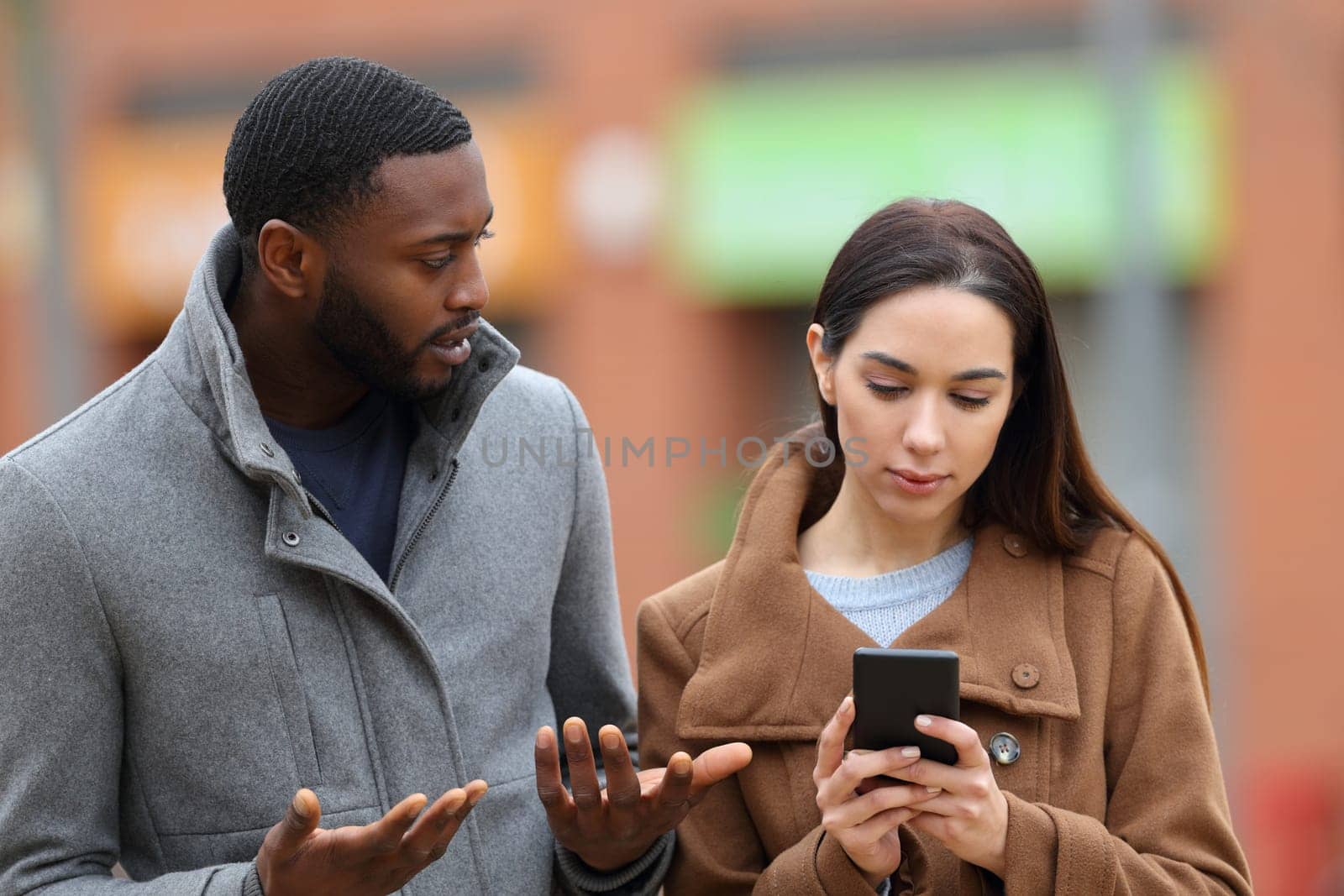 Woman using smart phone ignoring her friend in the street in winter