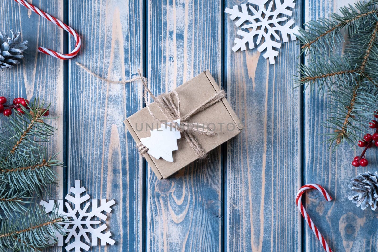 Kraft cardboard gift box tied with rough jute rope on gray wooden background with branches of Christmas tree and Christmas decorations. Top view