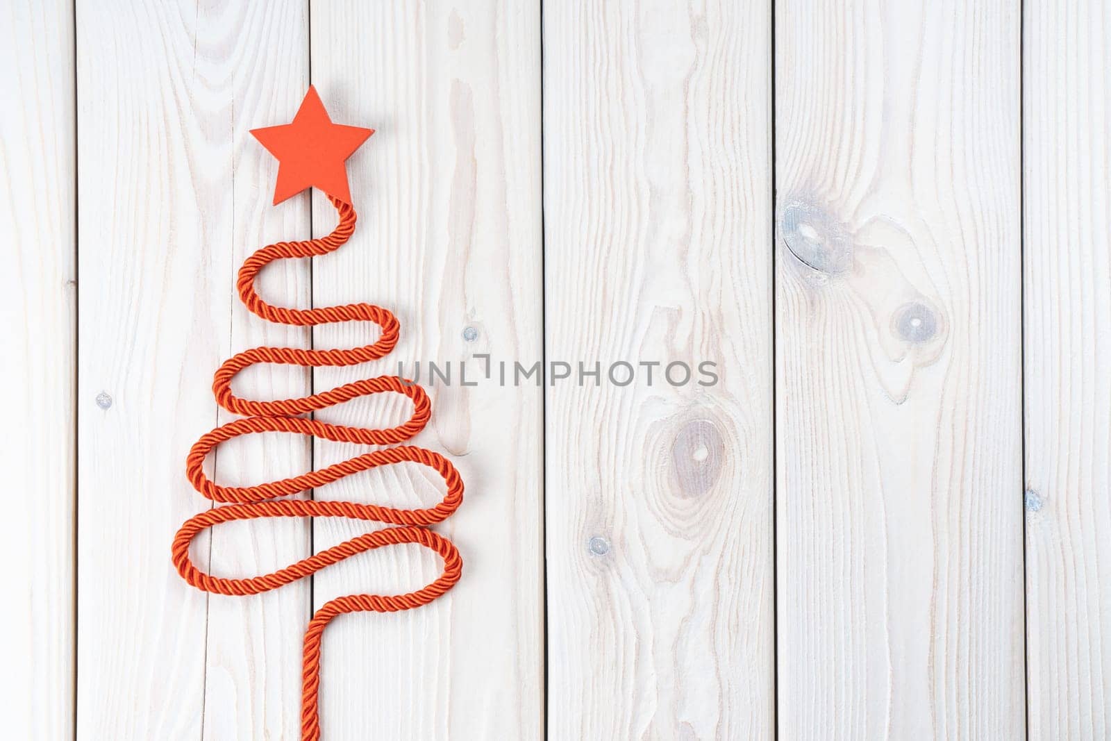 Red twisted cord folded in shape of Christmas tree with star on top. Fir tree on white wooden surface. Top view, copy space, place for text. Merry Christmas, Happy New Year greeting card