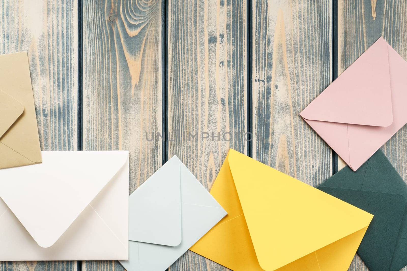 Multicolored envelopes lie randomly on gray wooden rustic textured background. Copy space. Place for text. Top view. Mail, correspondence, sending messages, congratulations