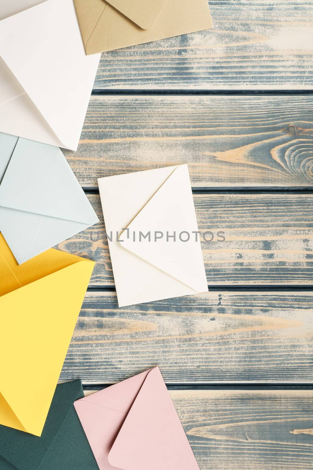 Multicolored envelopes lie randomly on gray wooden rustic textured background. Copy space. Vertical. Top view. Mail, correspondence, sending messages, congratulations
