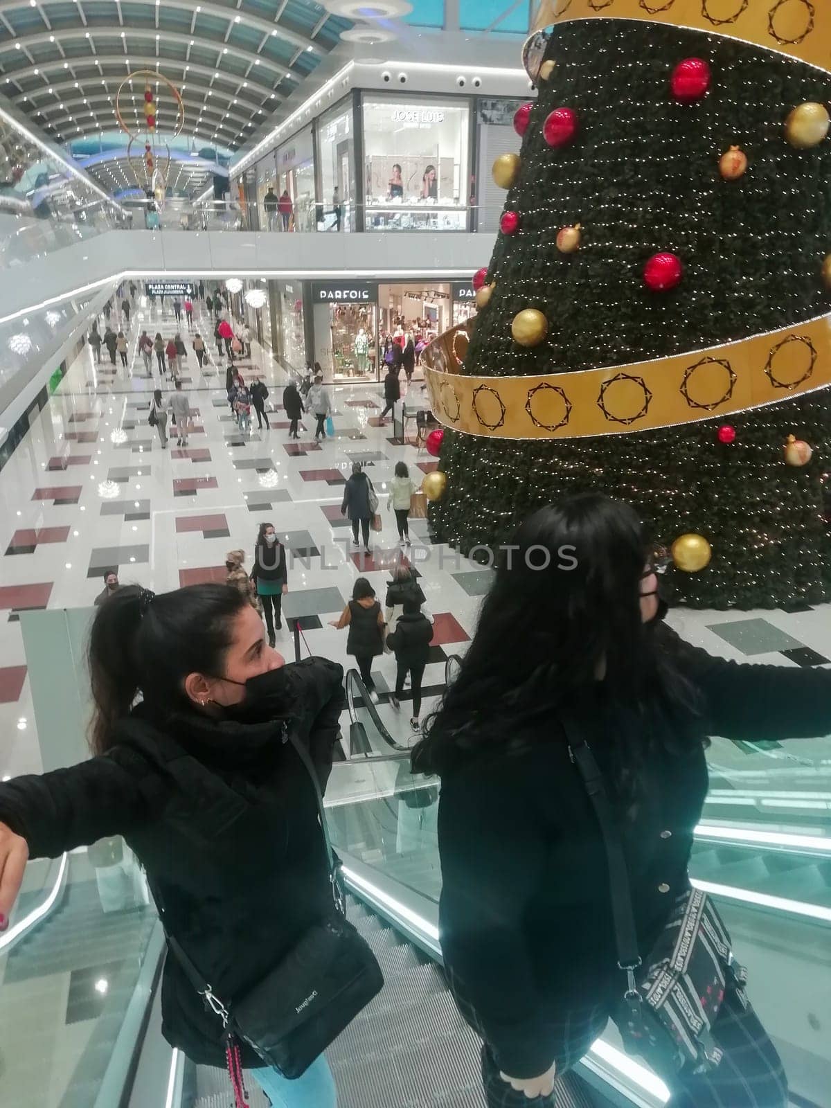 sierra nevada shopping centre, granada spain-december 22 2021: two women going up escalators in sierra nevada shopping centre during the winter sales looking at the big christmas tree.