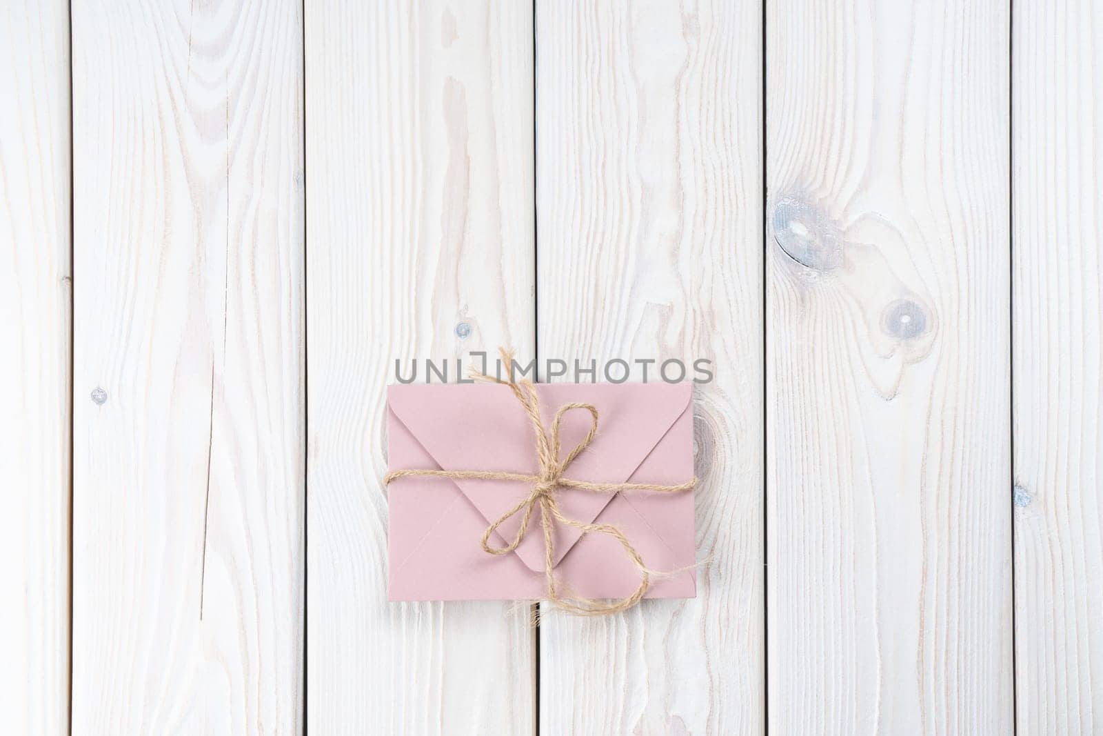 Pink envelope tied with rough jute rope on white wooden background. Copy space. Top view. Mail, correspondence, sending messages, congratulations