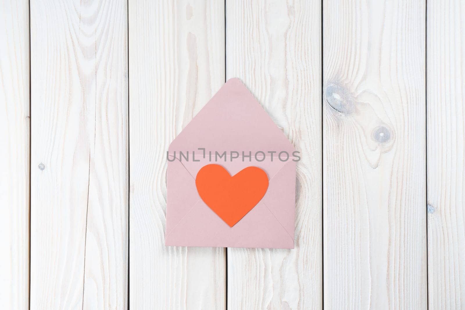 Pink opened envelope on white wooden background. Red cardboard heart is taken out of Valentine envelope. Copy space. Love, valentine, confession of feelings. Top view