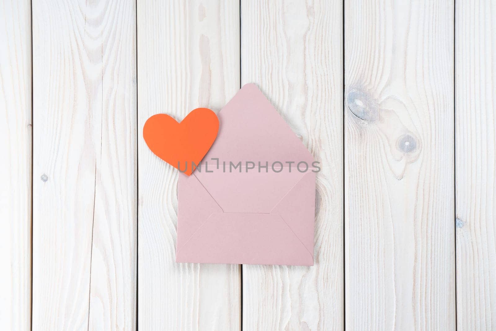 Pink opened envelope on white wooden background. Red cardboard heart is taken out of Valentine envelope. Copy space. Love, valentine, confession of feelings. Top view