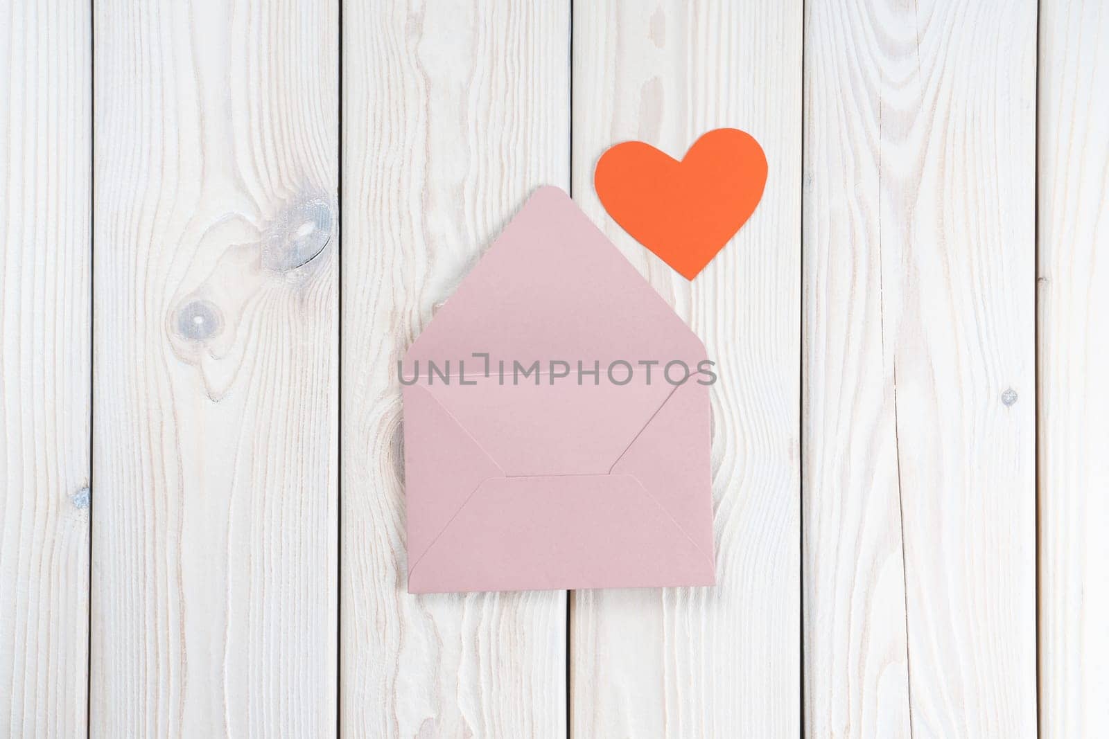 Pink opened envelope on white wooden background. Red cardboard heart is taken out of Valentine envelope. Copy space. Love, valentine, confession of feelings. Top view