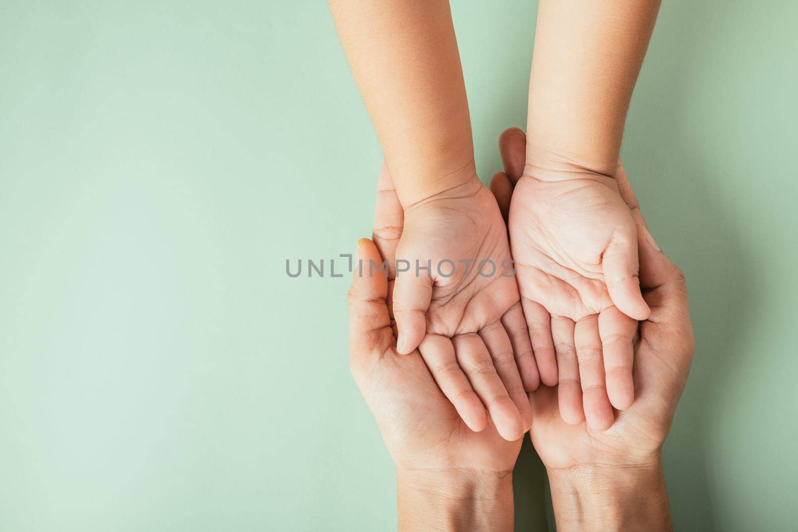 Closeup top view family hands stack palms studio shot isolated on green background, parents and kid holding empty free space on hand together, Gesture sign of support and love, Family and parents day