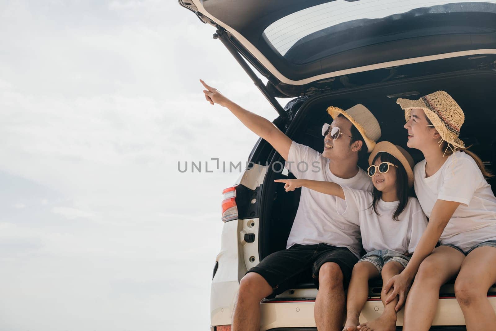 Happy Family Day. Family travel in holiday at sea beach, Dad, mom, daughter enjoy road trip sitting on back car and pointing finger out, people having fun in summer vacation on beach with automobile