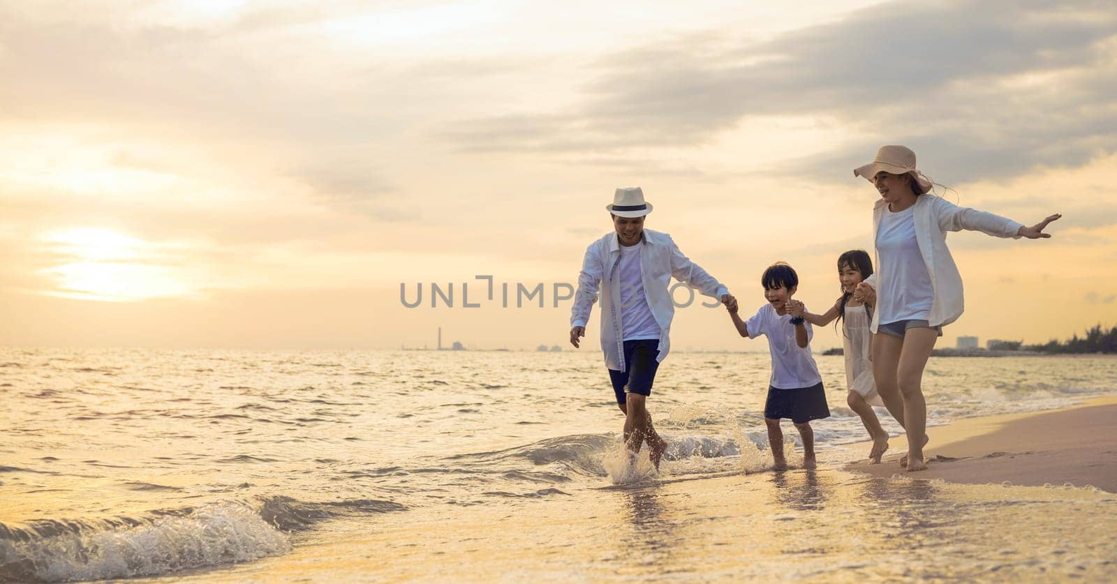 People of father, mother, children son and daughter family of four holding hands together walking outdoor, Happy family having fun running on a sandy beach at sunset, tropical summer travel vacations