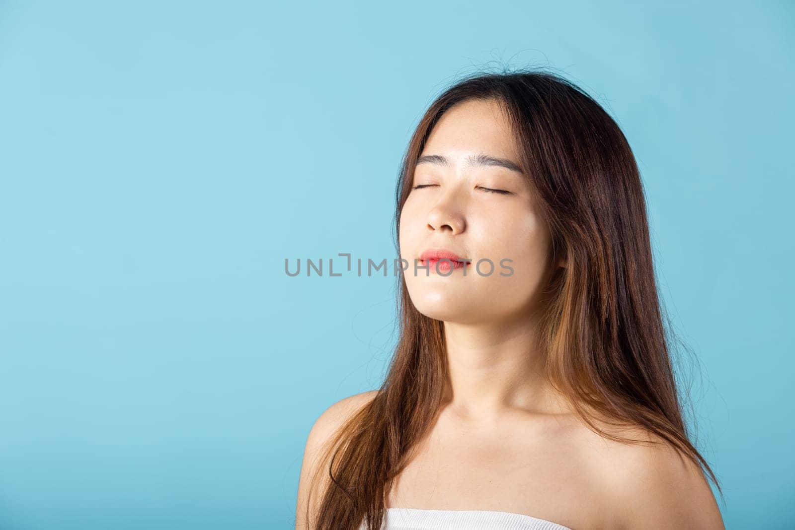 Front portrait of Asian young woman beautiful face closed eyes and smiling studio shot isolated on blue background, close up face of happy female healthy sleeping, beauty care calm and relaxed