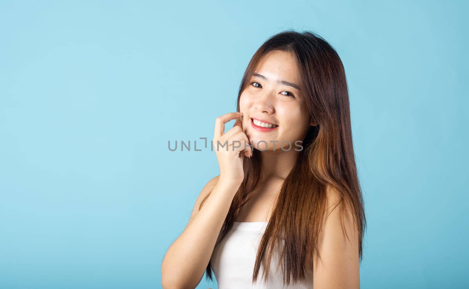 Skin care and Beauty concept. Portrait happy woman with natural makeup and healthy face studio shot isolated on blue background, Asian young female with beauty face touching healthy facial skin