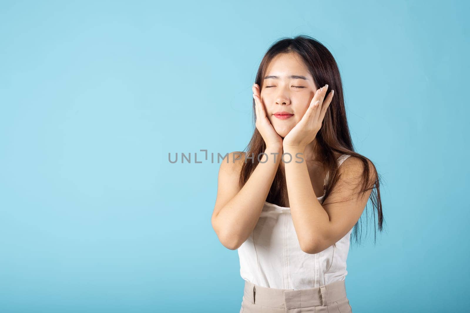 Beauty and Skin care. Beautiful woman model smiling with natural makeup and healthy face, Asian female with beauty face touching healthy facial skin studio shot isolated on blue background