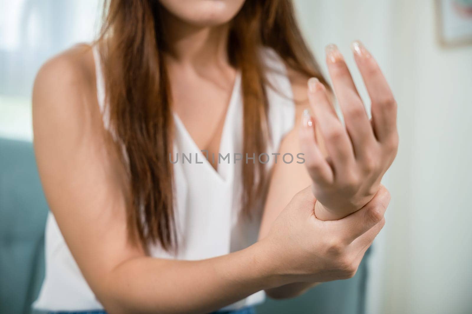 Closeup hand. Asian young woman sitting on sofa holds suffering her wrist at home, female hand injury feeling joint pain, performing self-massage, Health care and medical concept