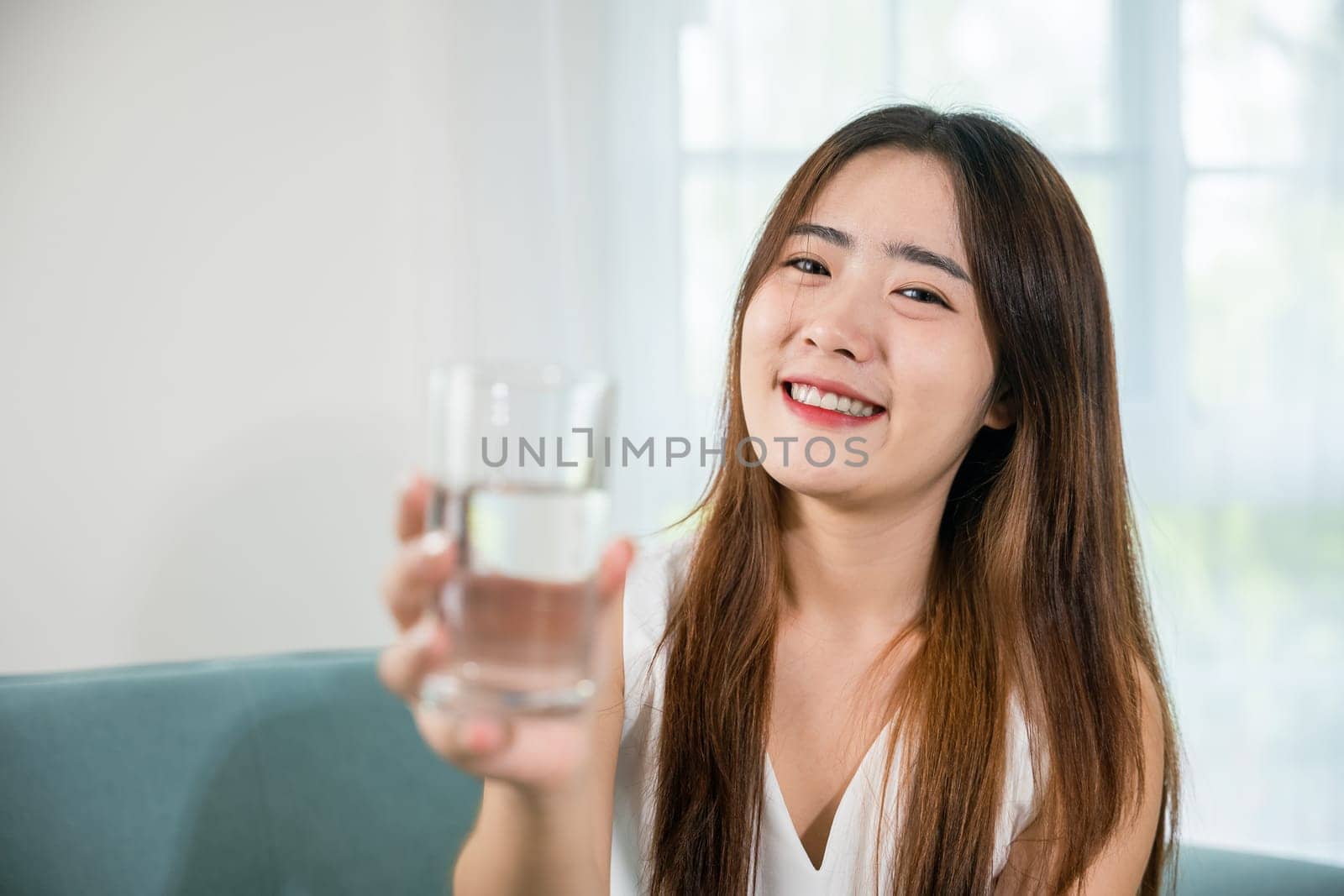 Portrait of Asian young woman holding drinking nature water on hand at home, Happy smiling female beauty with water glass for drink in living room, Healthy lifestyle