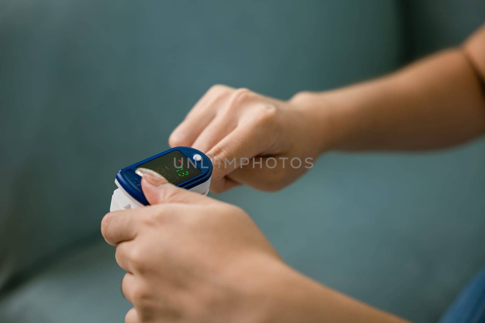 Young woman using pulse oximeter to monitor blood oxygen levels and pulse rate on finger under sofa in living room at home, Self healthcare with coronavirus pandemic, medical healthcare concept