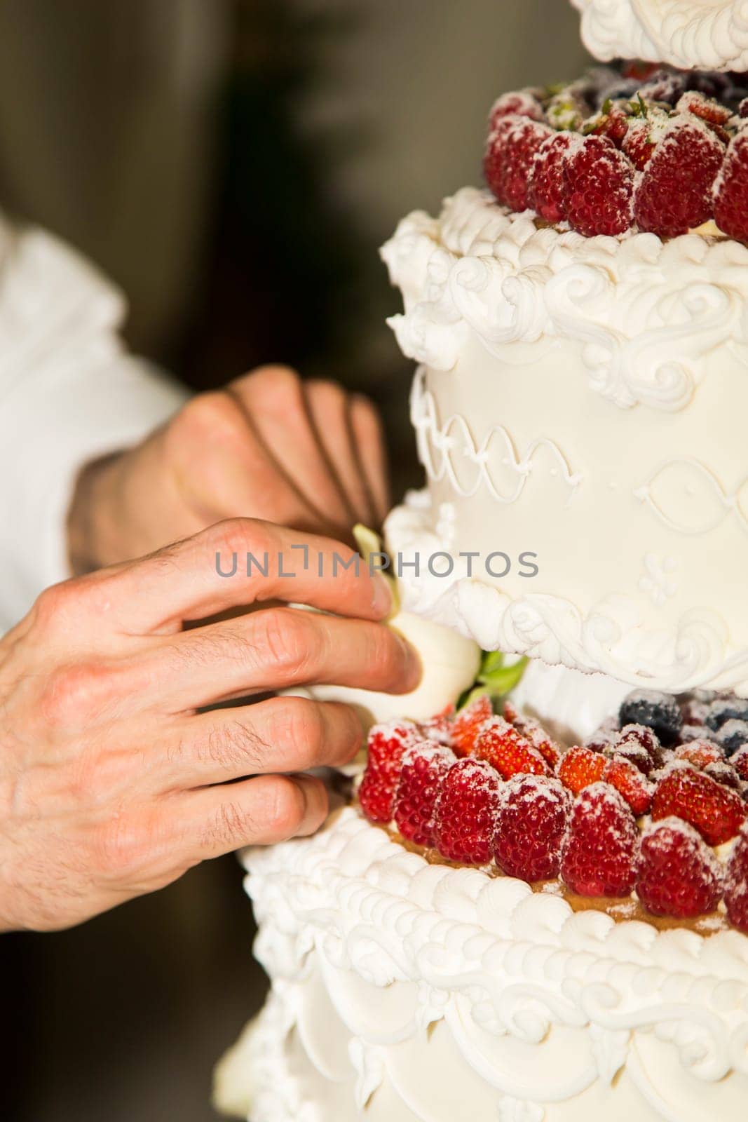 Close-up view of the hands of a baker whereas wedding cake adorned