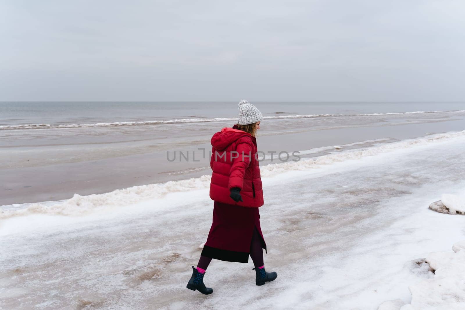 A woman in warm clothes walks along the sea in winter.