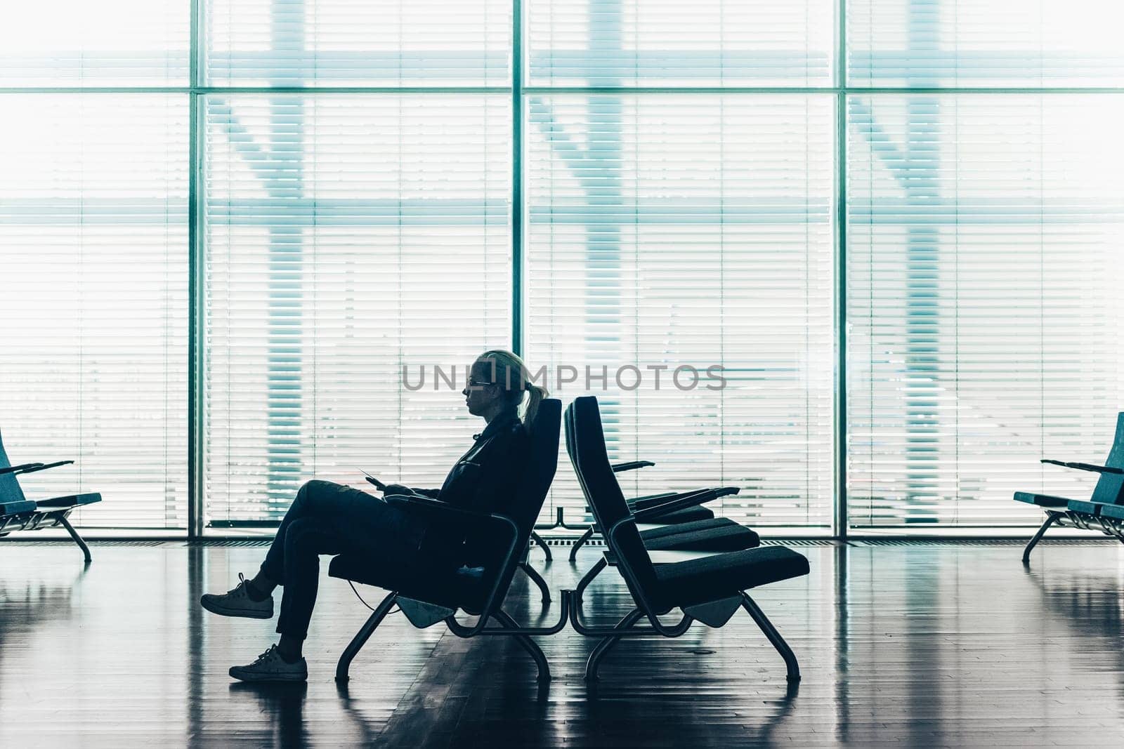Silhouette of a woman in transit using smarthphone, waiting on airport gate. Horisontal composition. Focus on passanger.