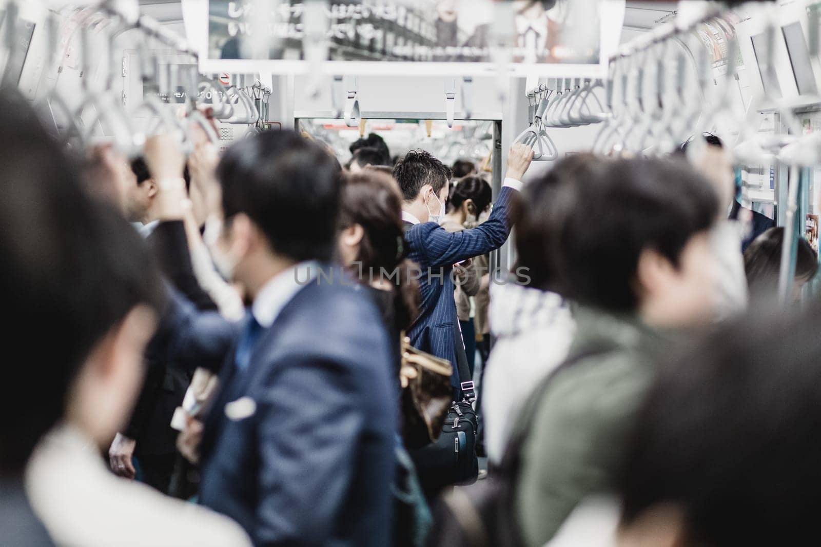 Passengers traveling by Tokyo metro. Business people commuting to work by public transport in rush hour. Shallow depth of field photo. Horizontal composition.