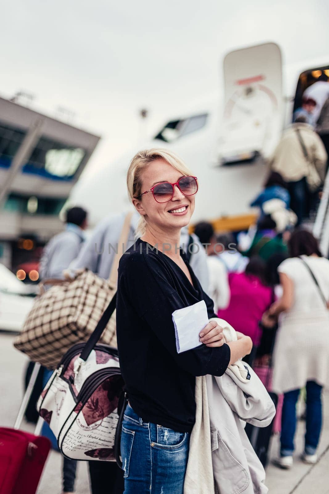 Cheerful woman holding carry on luggage queuing to board the commercial airplane.