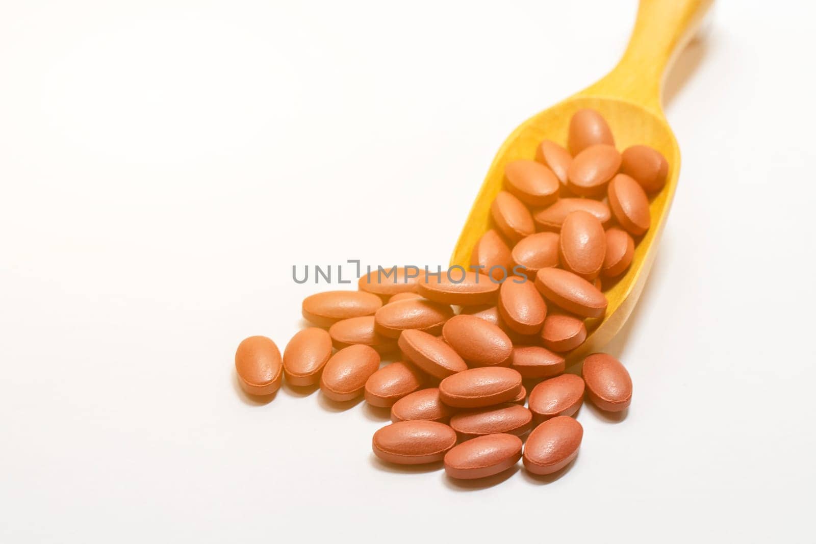 Ferrous fumarate or vitamins on wooden spoon on white background