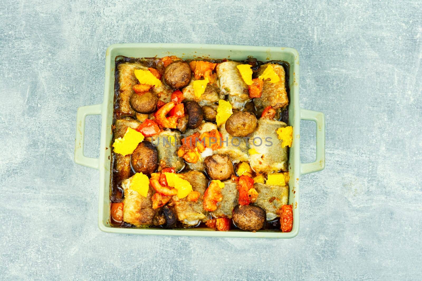 Fried hake fish grilled with orange, tomato and mushrooms. Close up