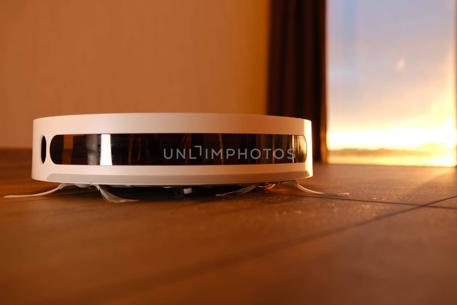white vacuum robot cleaner close up with sunset light on the brown dalle with beautiful flares and dust around.