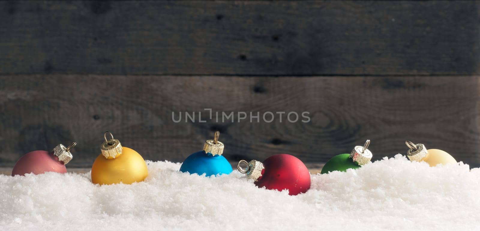 Colorful Christmas baubles in the snow, wooden background with space for text, seasonal backdrop