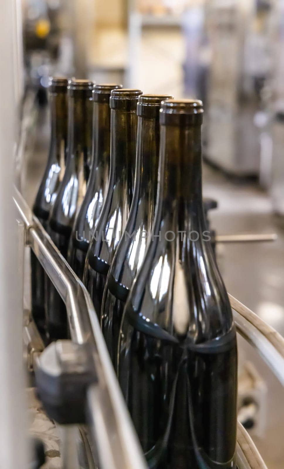 Dark glass bottles being filled with wine by industrial bottling machine at modern wine factory in Italy. Automatic conveyor line for wine-producing