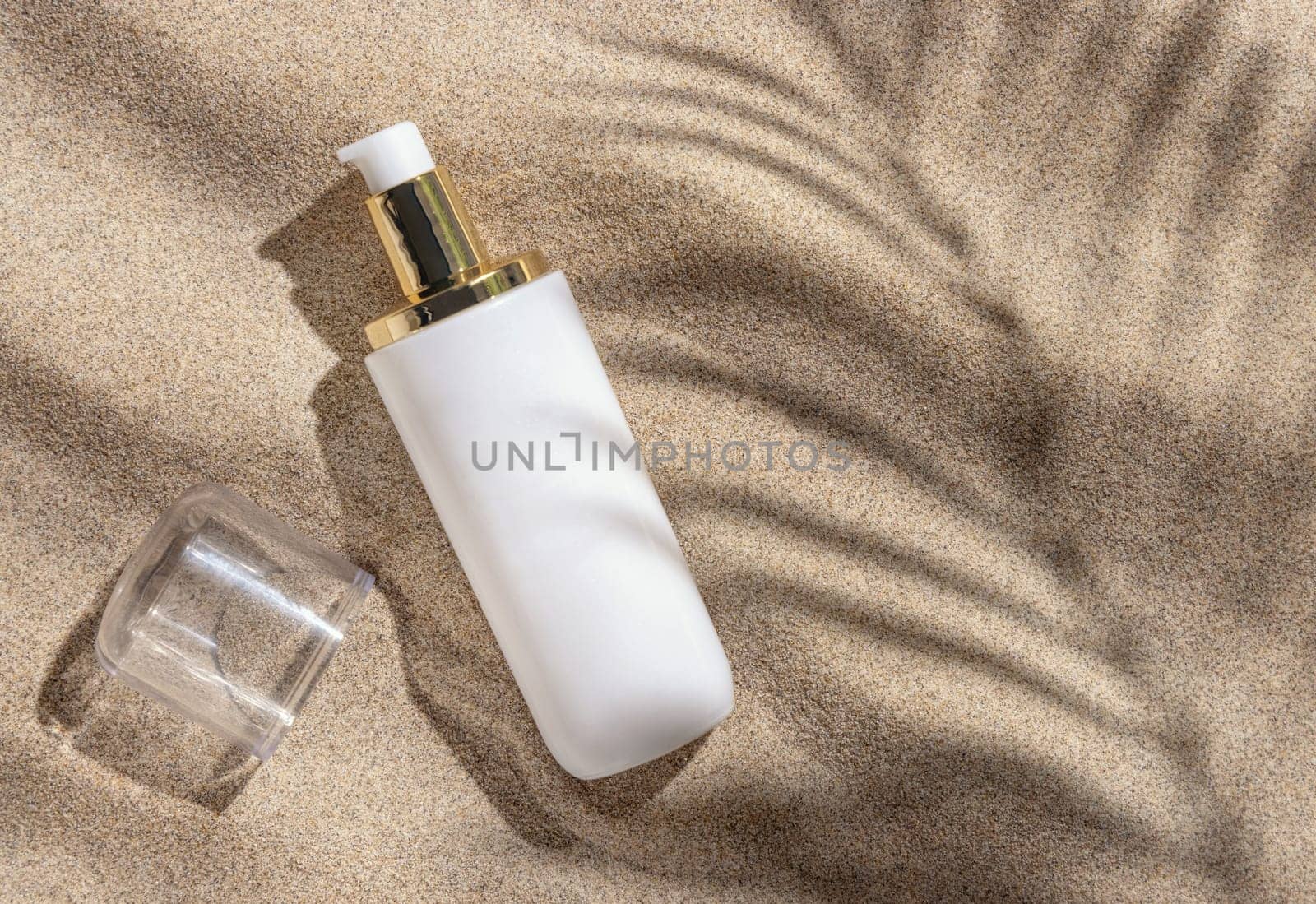 Blank white one pump cream bottle on beige sand top view. Packaging mockup. Natural skincare product for beauty routine. Summer sunny day with palm leaf hard shadow, tropical vacation mood
