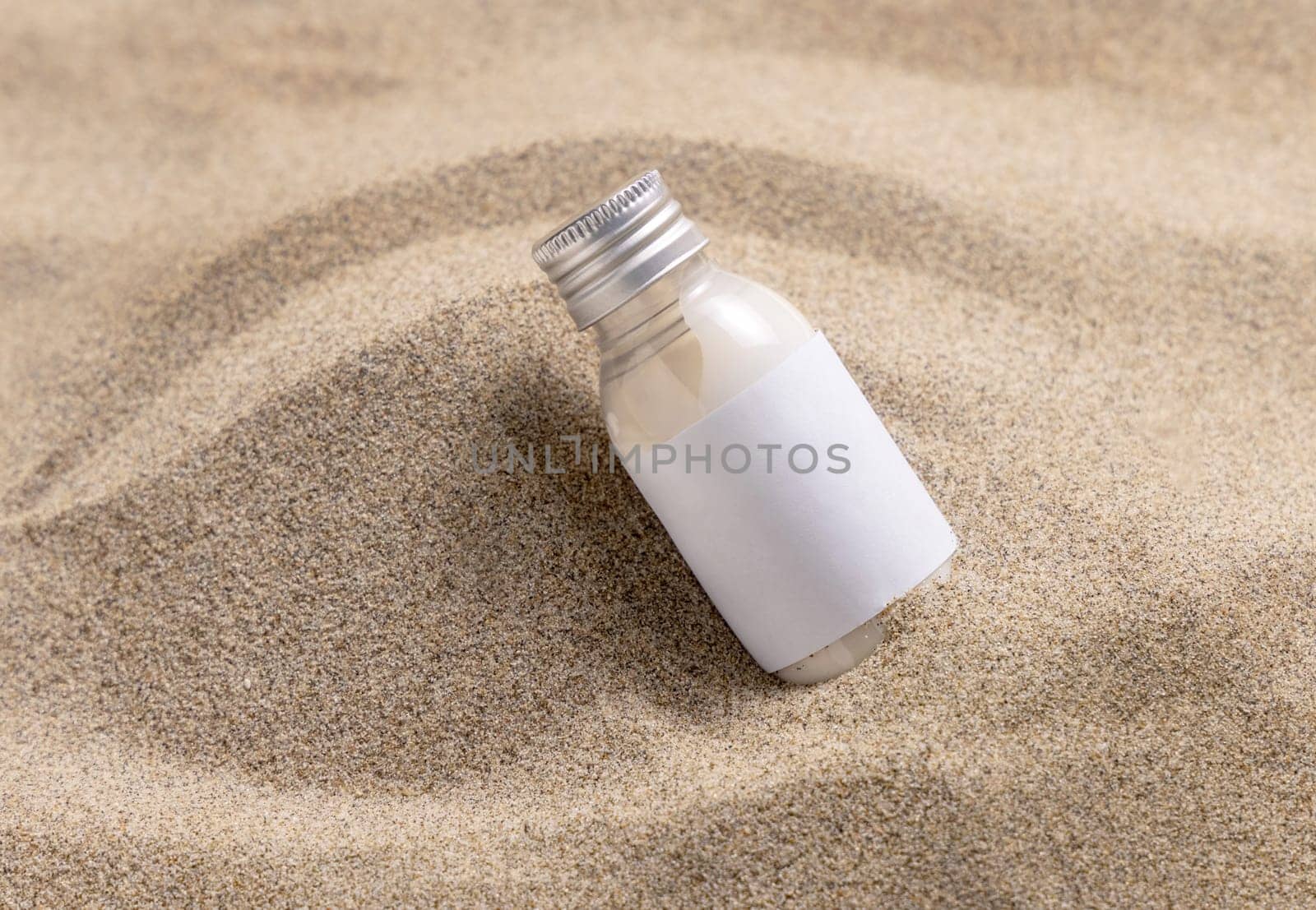 Blank Cream bottle with blank label on beige sand close up. Cosmetic packaging mockup. Natural skincare product for beauty routine. Summer tropical vacation mood