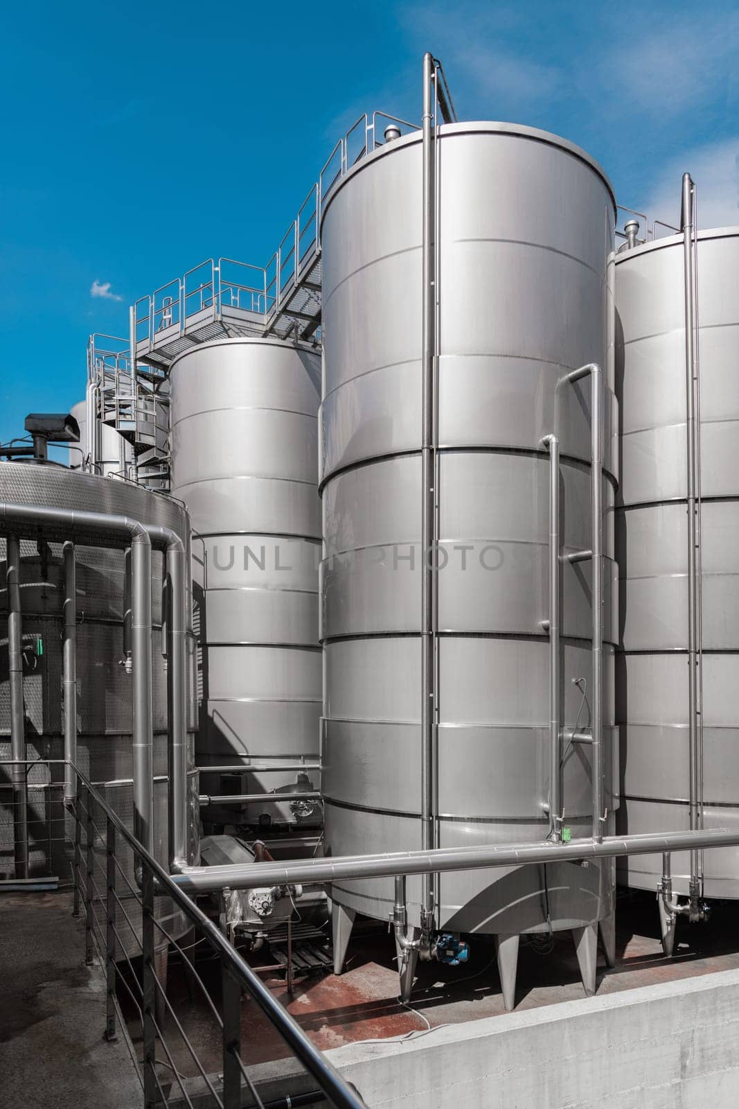 A row of steel wine tanks for wine fermentation at a modern winery. Large brewery silos typically used for storing barley or fermeted beer against blue sky.
