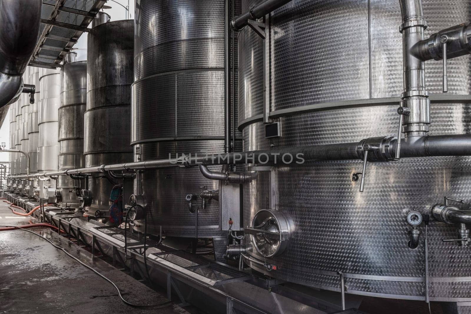 A row of steel wine tanks for wine fermentation at a modern winery. Large brewery silos typically used for storing barley or fermeted beer against blue sky.