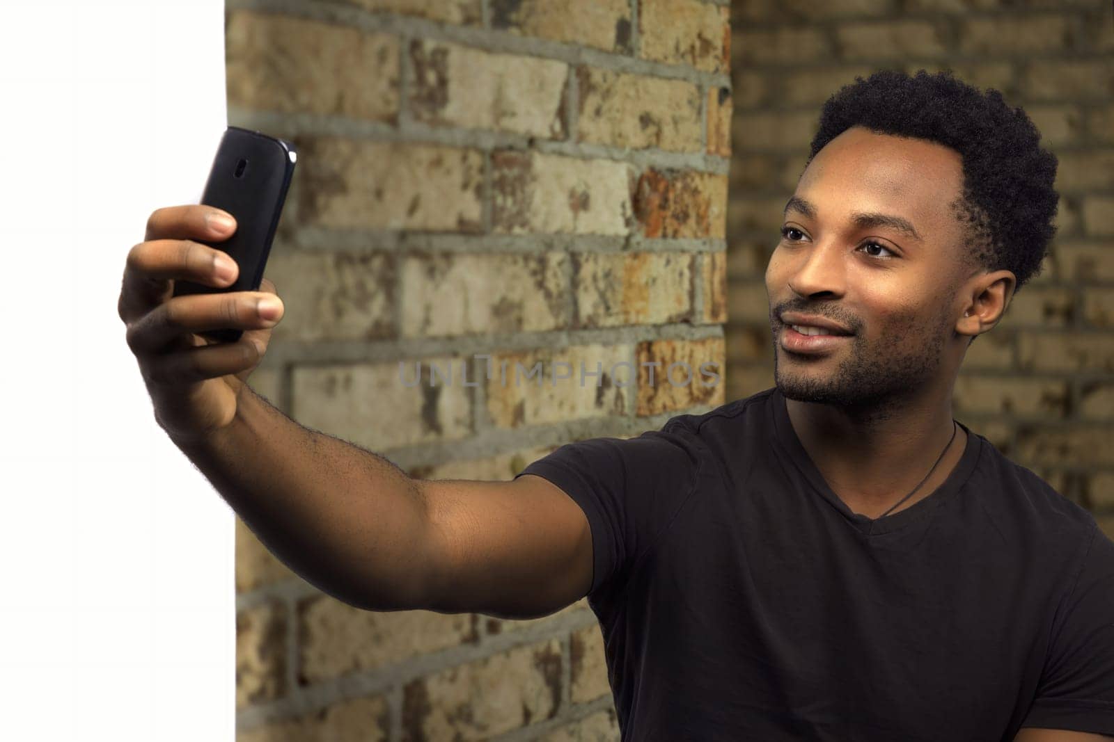 selfie taking young man holding smartphone and smiling for camera student social network brick and white wall