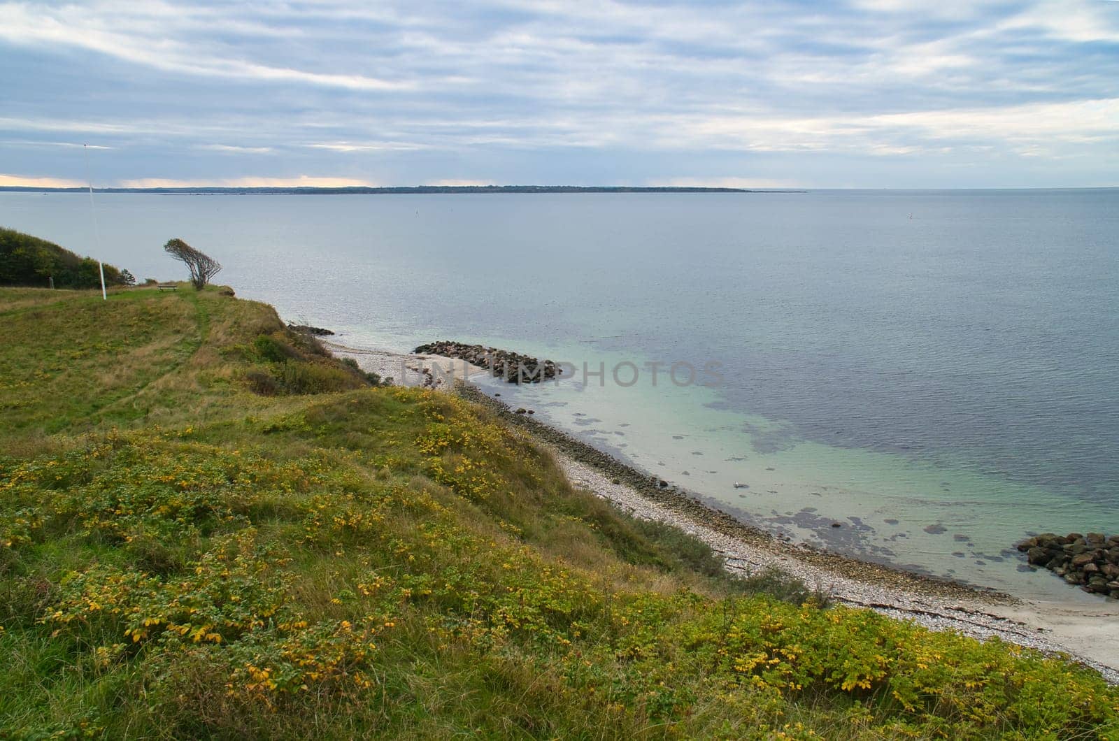 Hundested, Denmark on the cliff overlooking the sea. Baltic Sea coast, grassy meadow, beach. Clouds on horizon. Landscape photo from Scandinavia.
