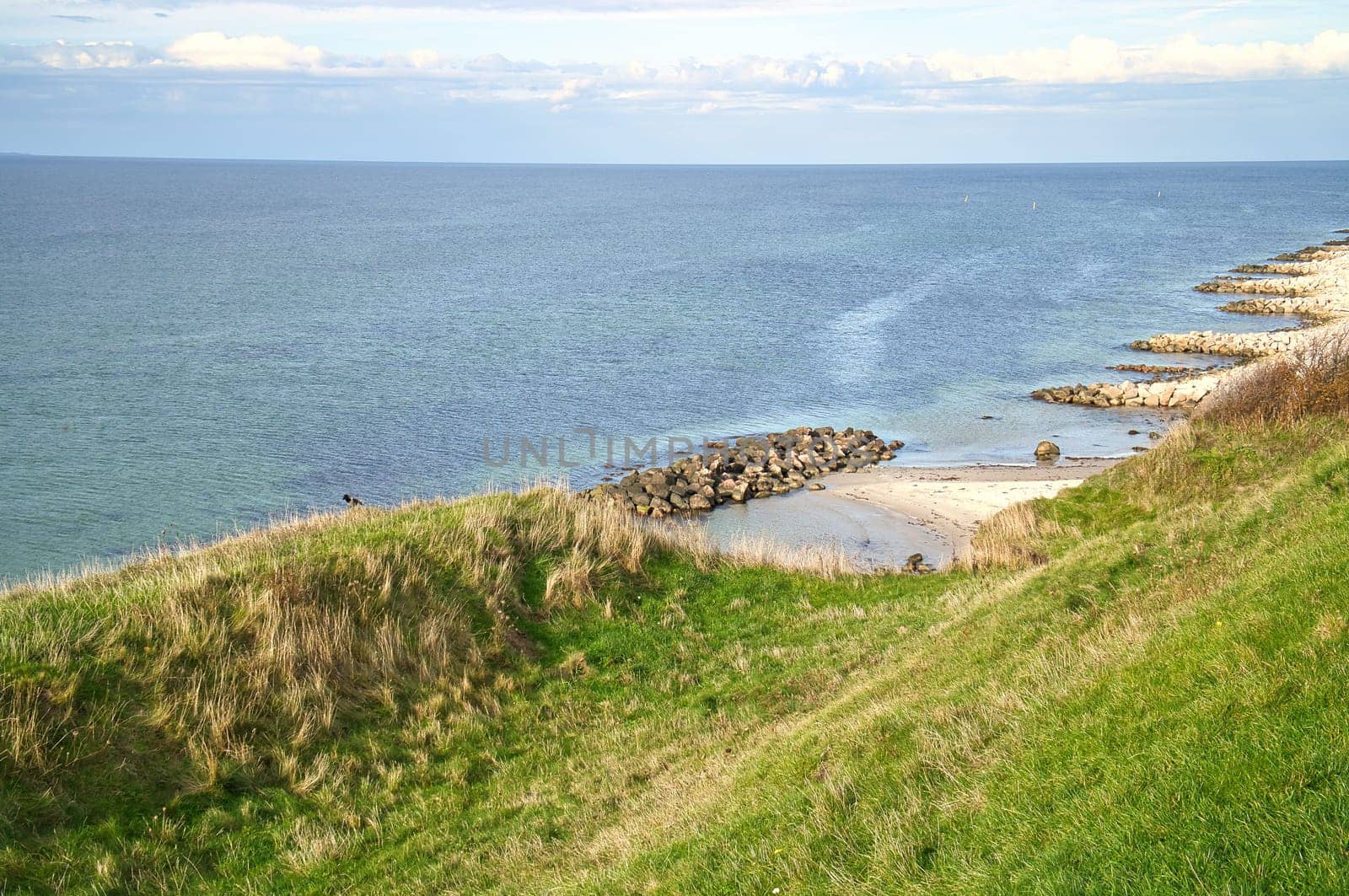 Hundested, Denmark on the cliff overlooking the sea. Baltic Sea coast, grassy meadow, beach. Clouds on horizon. Landscape photo from Scandinavia.