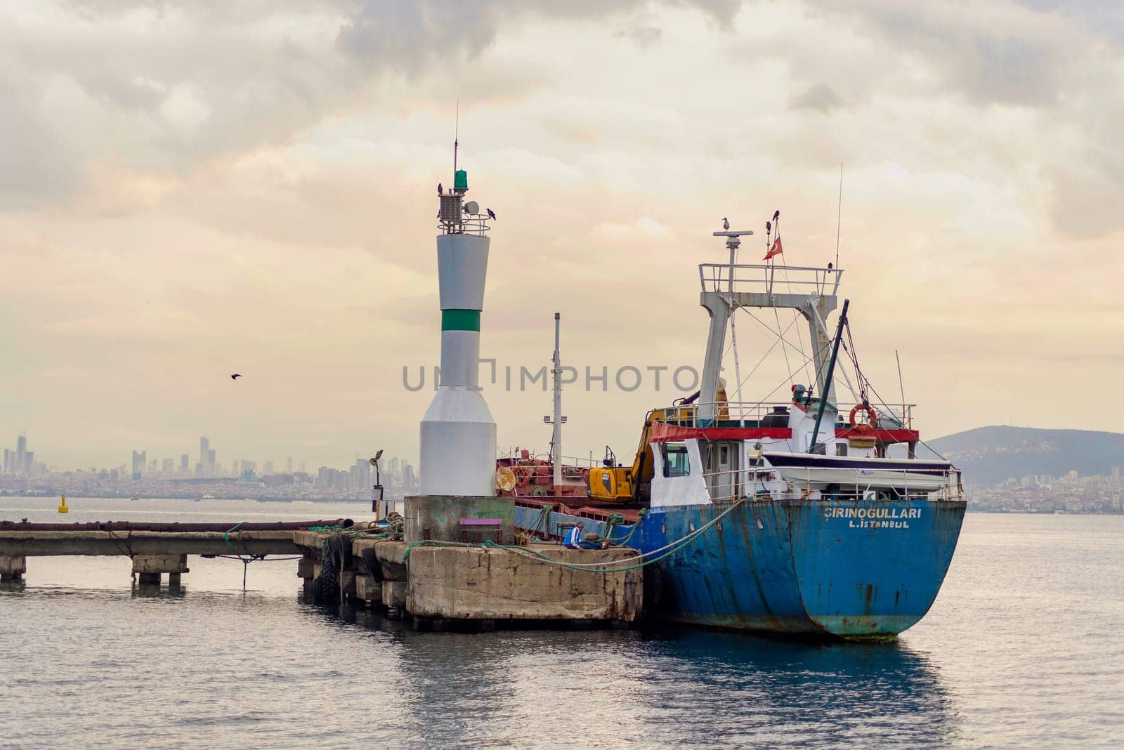 Old cargo ship docked beside a small beacon, at Kinaliada island harbour, marmara sea, near Istanbul, Turkey, at sunrise, in a summer day