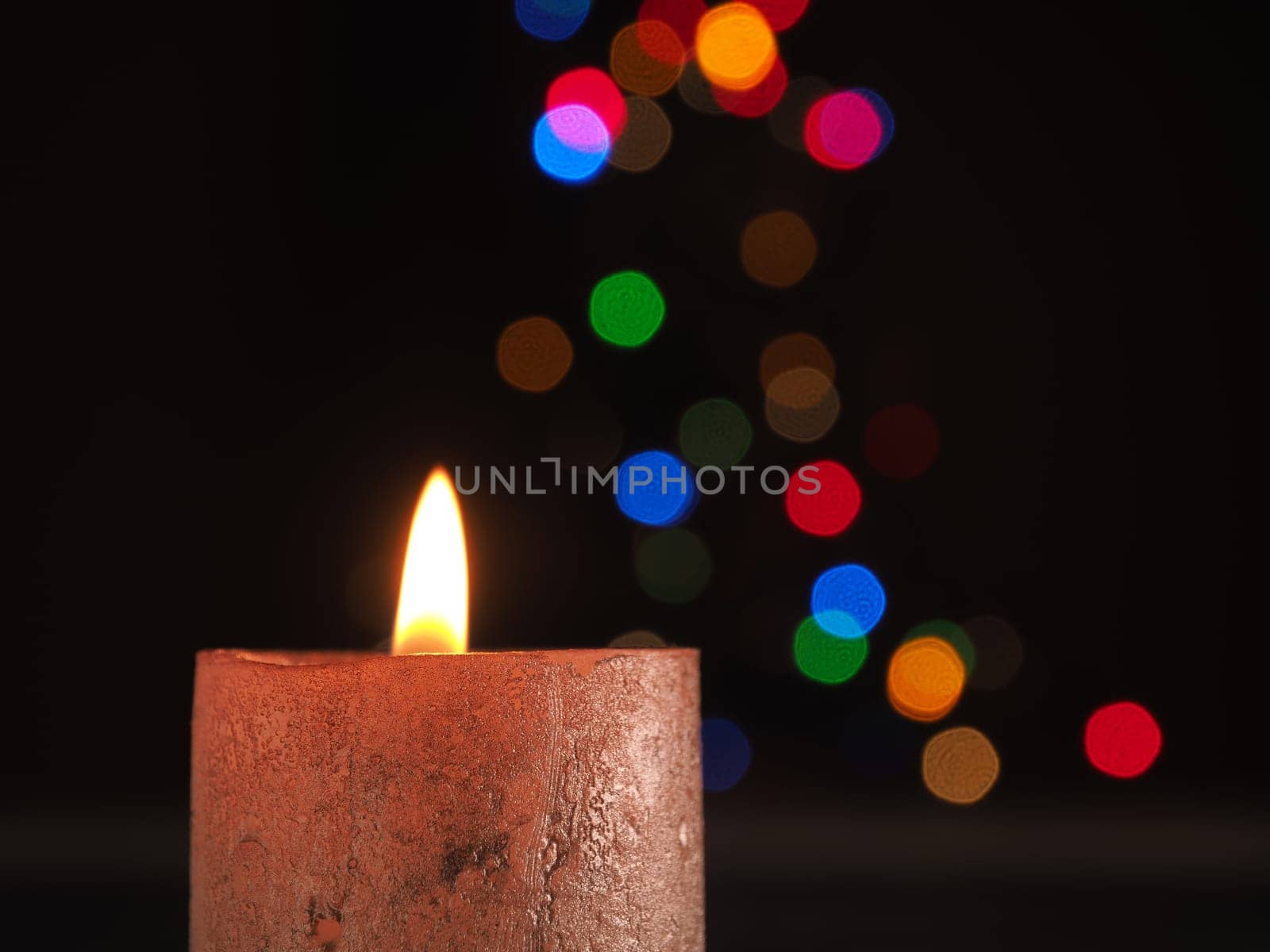 First Advent candle burns with Christmas lights bokeh and space for text